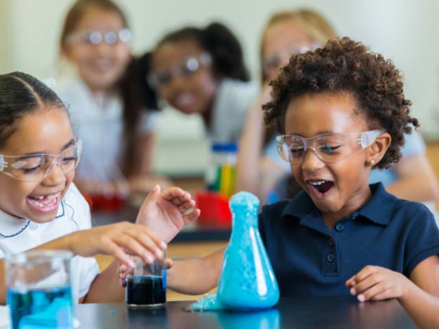 Two young students laughing watching a beaker overflow during a science expeeriment