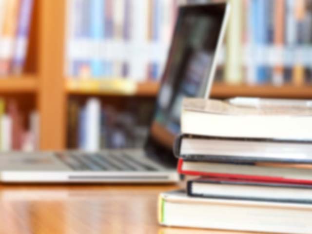 Stack of books on a table in front of a laptop