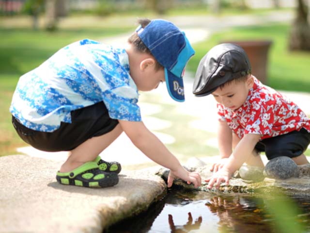 Two young boys playing together, reaching into a pond