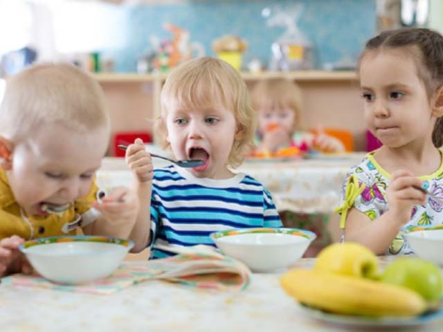 Two young boys and a little girl eating their lunch together