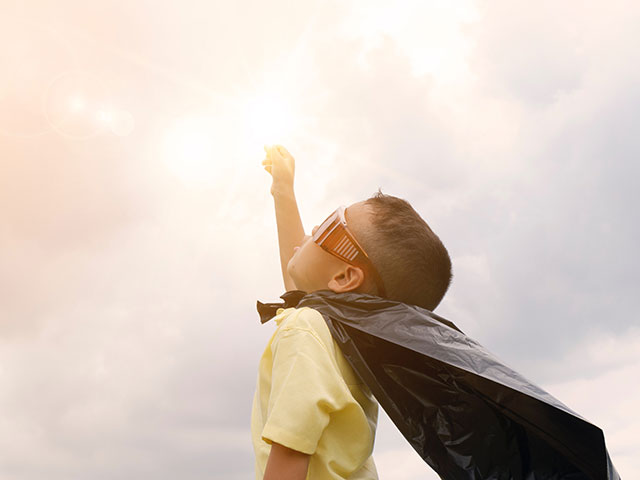 Young child dressed as a superhero pointing to the sky